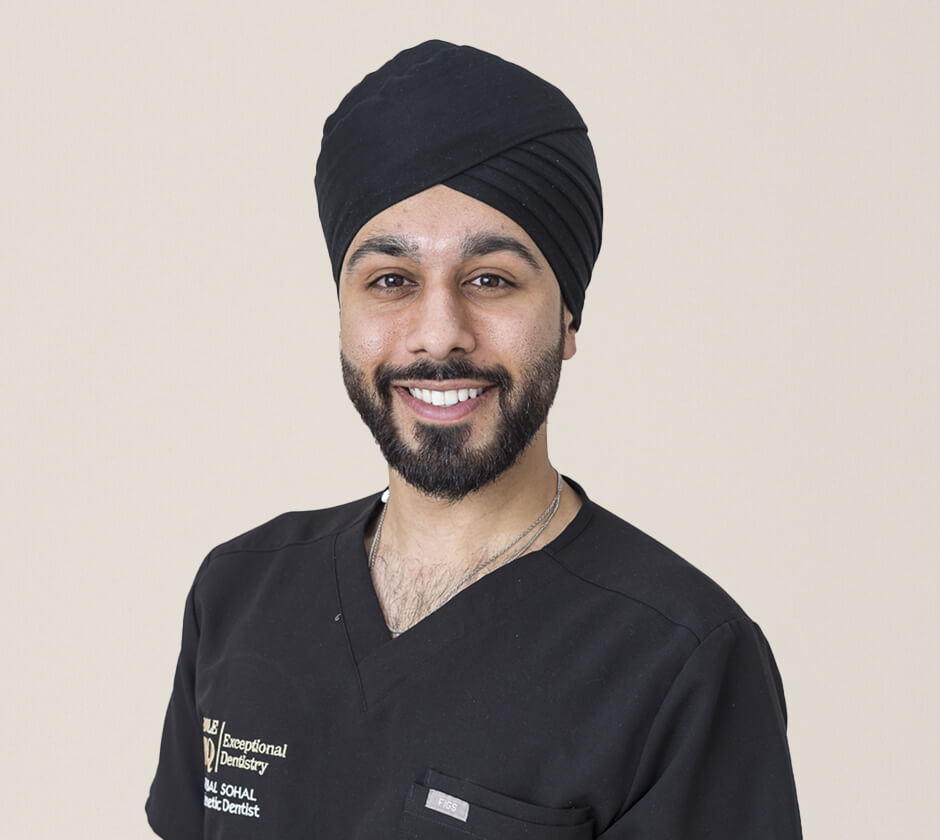 A smiling dentist wearing a black turban and a black medical scrub shirt.