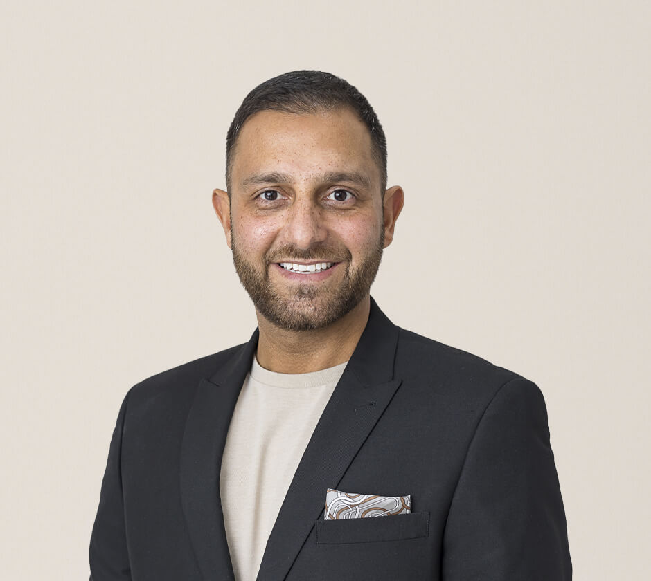 Portrait of a smiling dentist wearing a black suit and beige shirt.