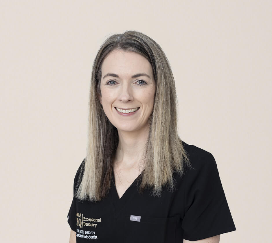 A portrait of a woman in black dental scrubs, smiling confidently. She is a specialist endodontist at Smile HQ.