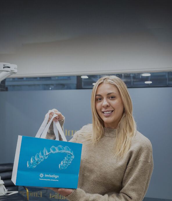 Image of a smiling woman holding an Invisalign bag, showcasing her dental treatment at Smile HQ Exceptional Dentistry.