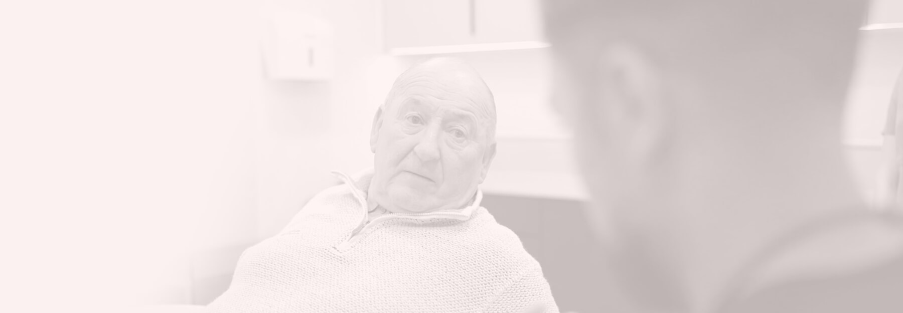 An elderly patient is sitting in a dental chair, looking at the dentist.