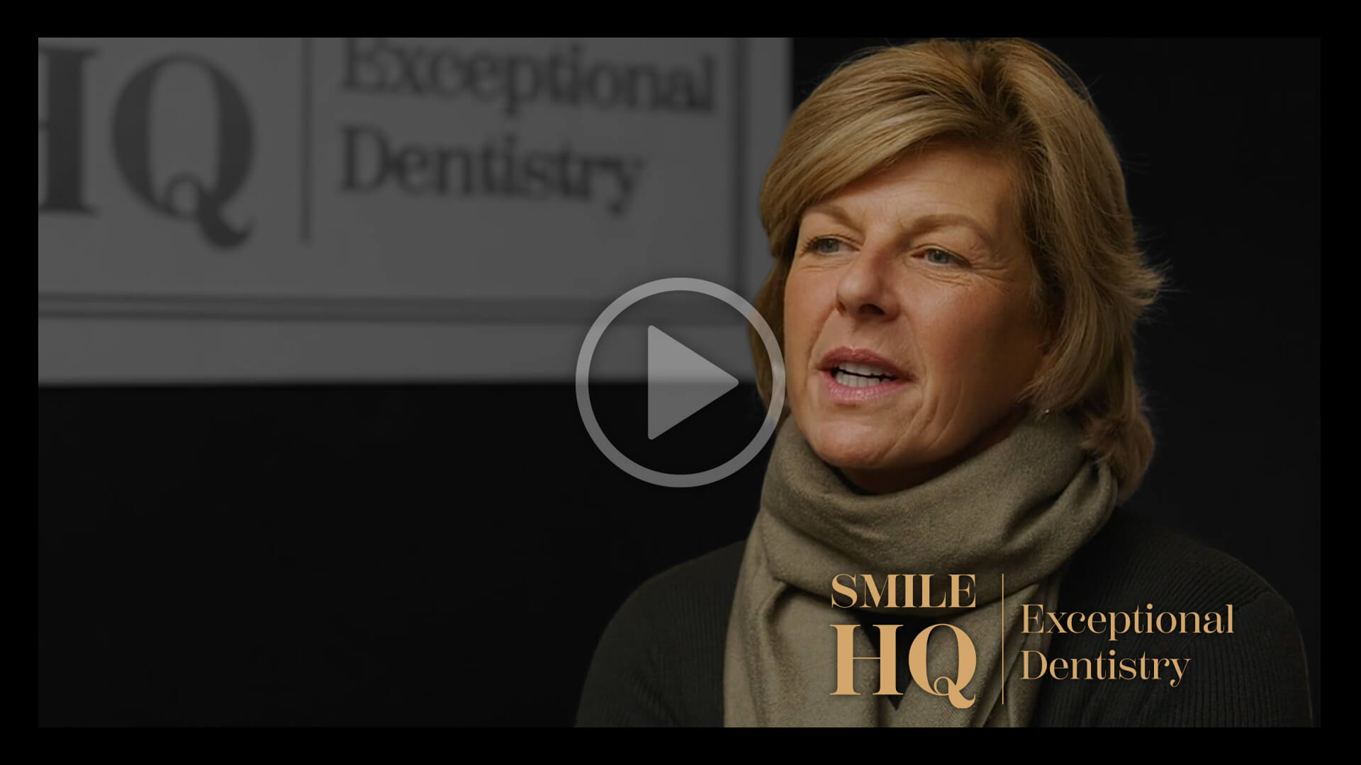 A woman wearing a beige scarf is sitting in front of a dark background, speaking in a patient interview for Smile HQ
