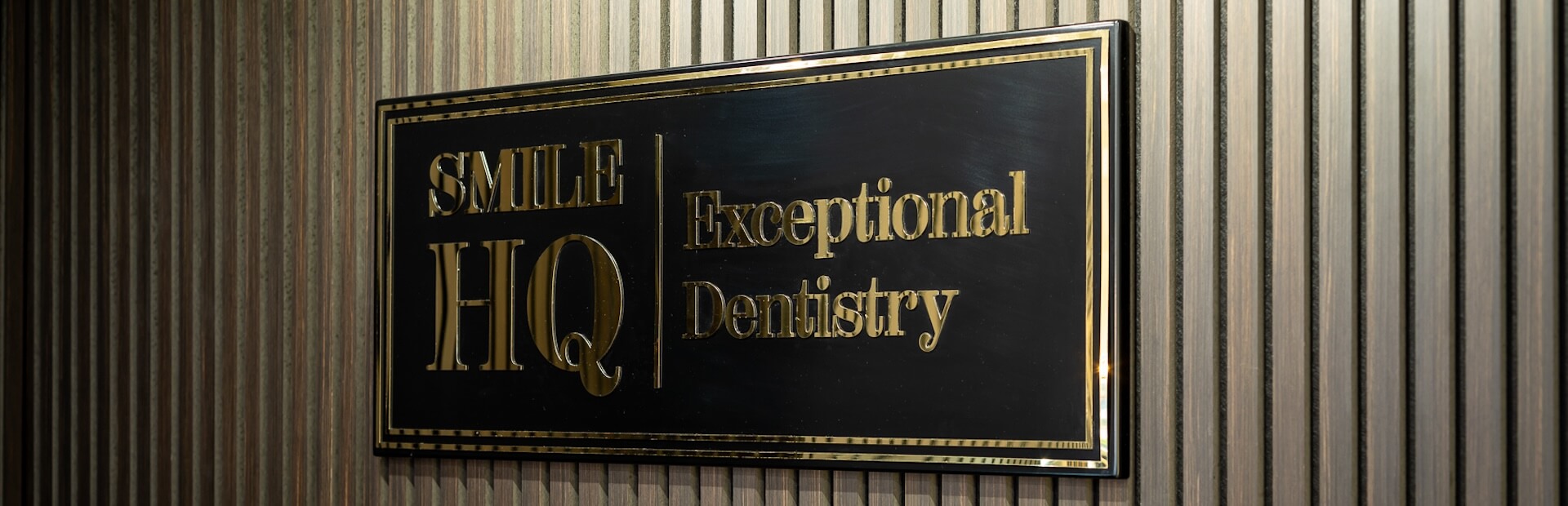 Close-up of the "Smile HQ Exceptional Dentistry" sign on a textured wall.