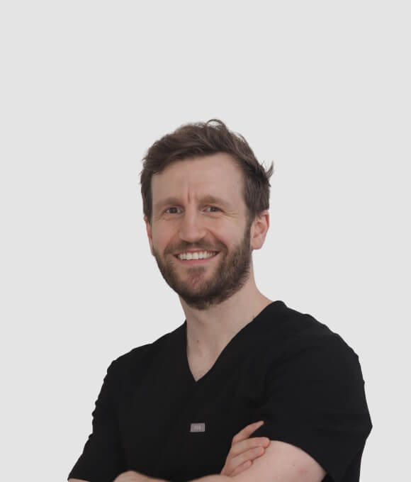 Portrait of a smiling dentist in a black scrub, standing with arms crossed.