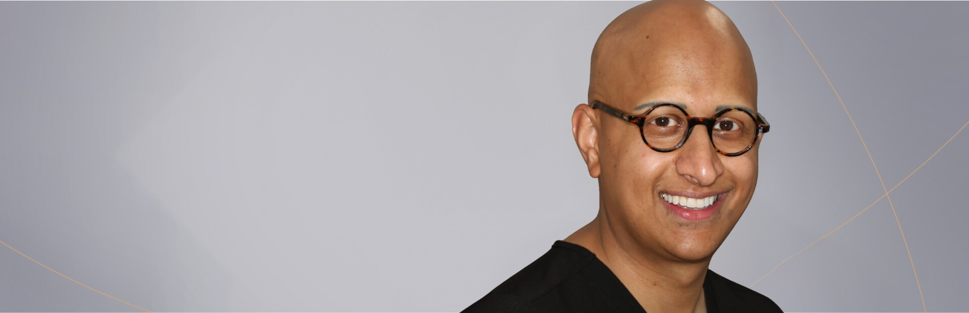Portrait of a smiling dentist wearing glasses and a black dental scrub.