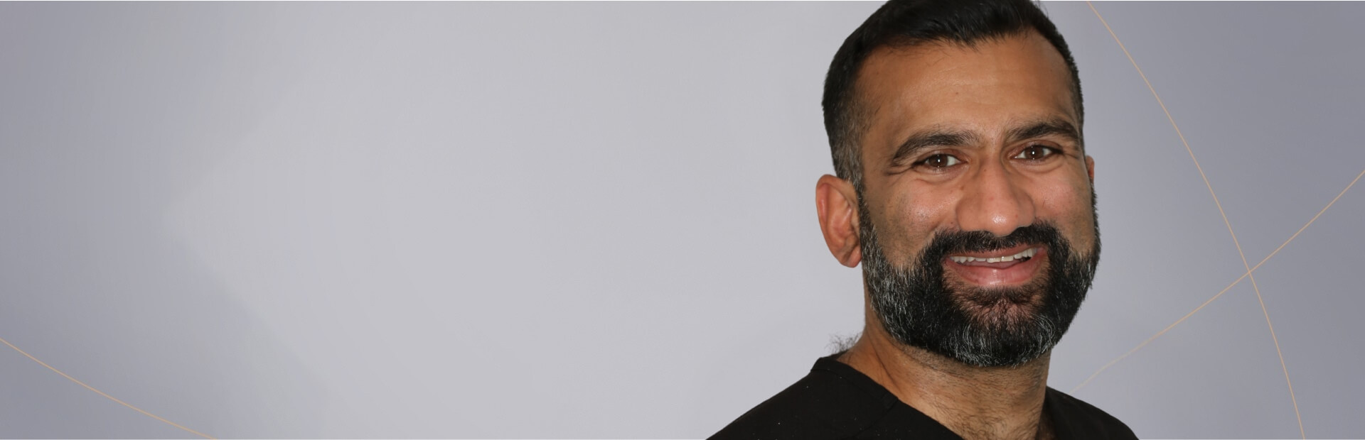 A portrait of a man in black dental scrubs, smiling and displaying a full beard. He is a member of the Smile HQ.